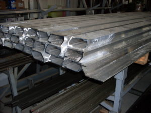 Húzott alumínium szelvények (fent), melyekből darabolással kialakítható a lengőajtó fogantyú és négyszög acélrudak (lent), melyekből az ajtókilincs és ablakkilincs tengelyek készülnek